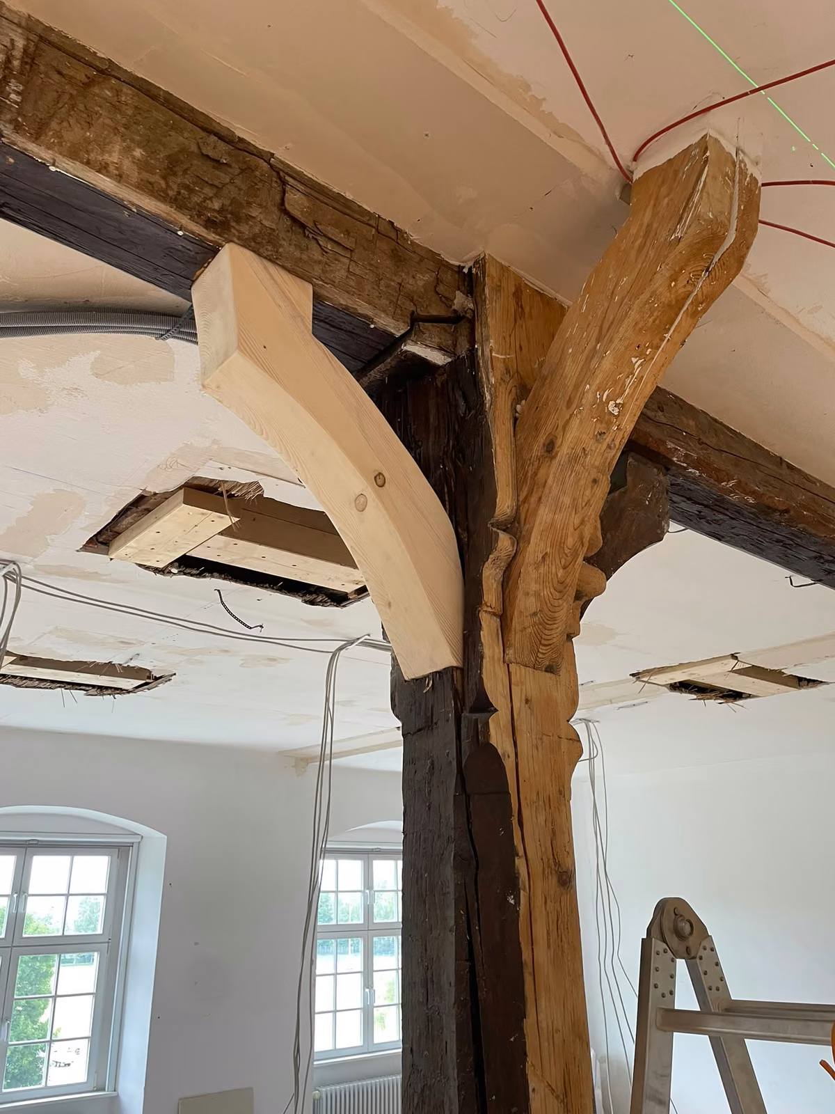 Historische Holzstütze mit zwei Kopfbändern: links ein neu gefertigtes, helles Kopfband, rechts das dunkle, geschnitzte Original